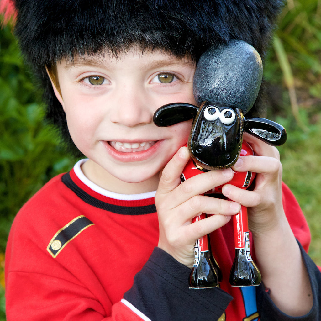 Guardian Shaun the Sheep figurine held by a smiling child dressed as a king's gaurdman. 