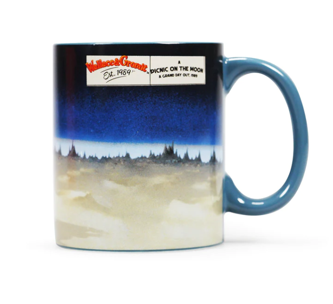 Mug with a blue handle, featuring a scene from Aardman's 'A Grand Day Out film'. Pictures Wallace holding a picnic basket and kicking a ball with Gromit by his side. The iconic orange rocket is in the background. 