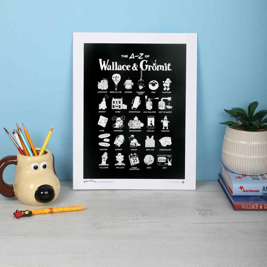 Print titled 'The A-Z of Wallace & Gromit' on a table with stationery items.