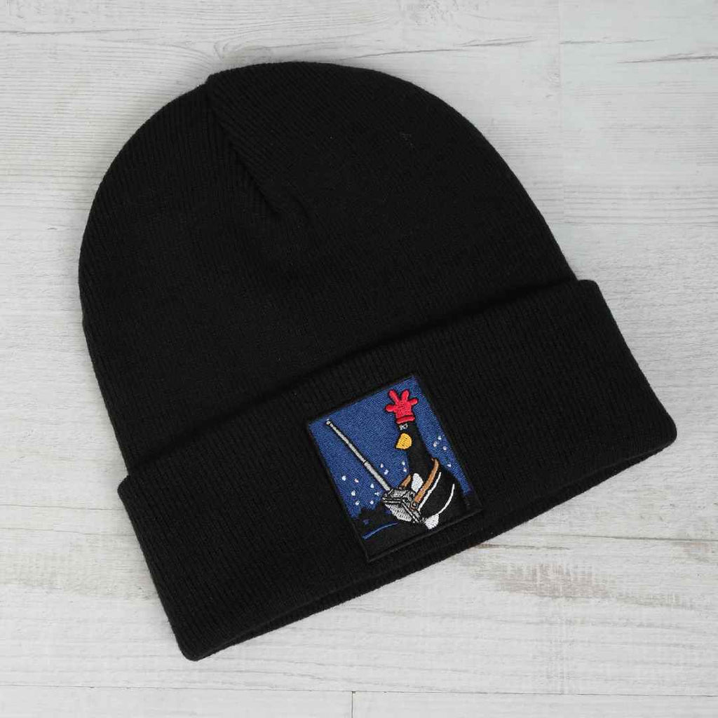 Black beanie with a colourful  Feathers McGraw  with his remote control patch on a light wooden surface
