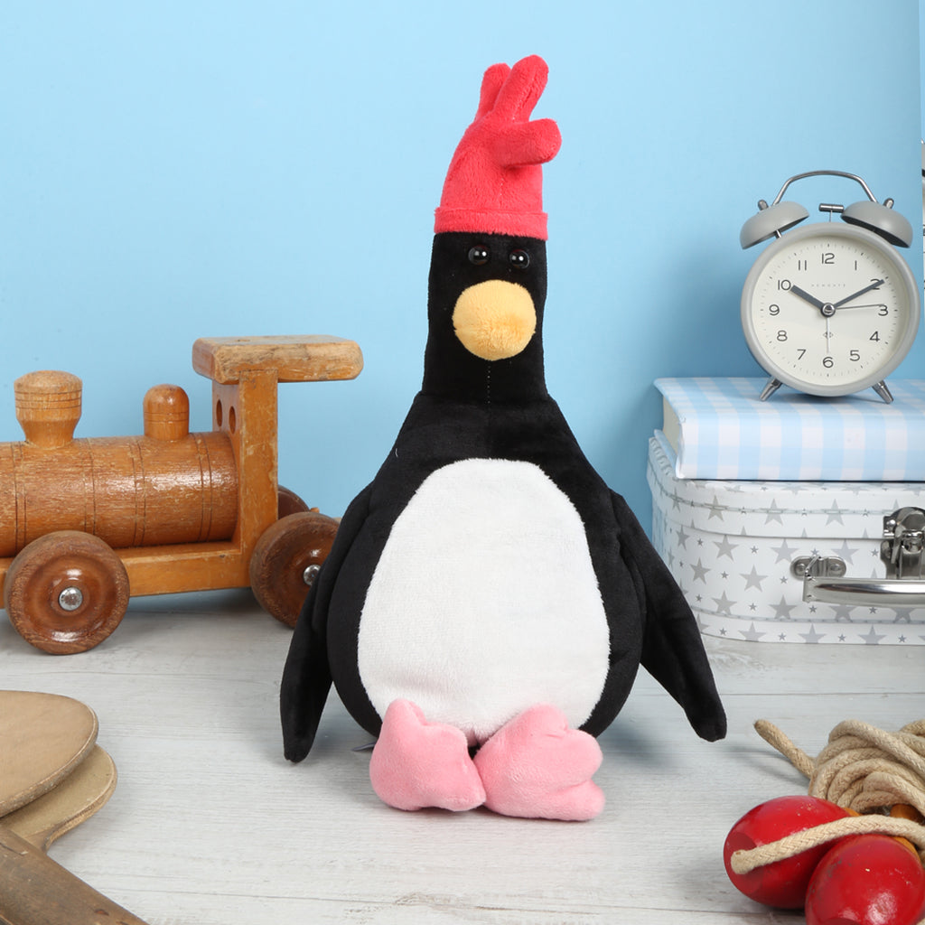 Feathers McGraw Microwavable Plush Toy with a redhat on a wooden floor with toys and a clock in the background.