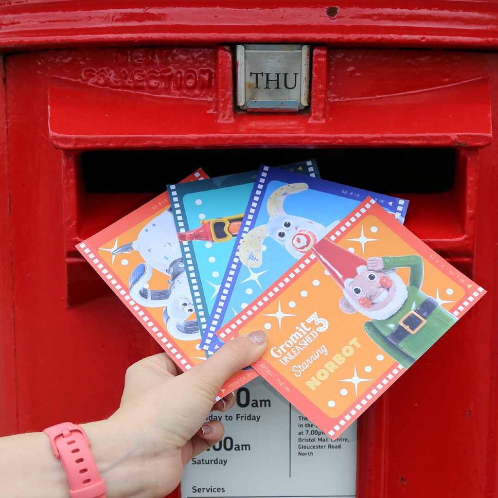 Hand placing colourful Gromit Unleashed 3 postcards into a red postbox