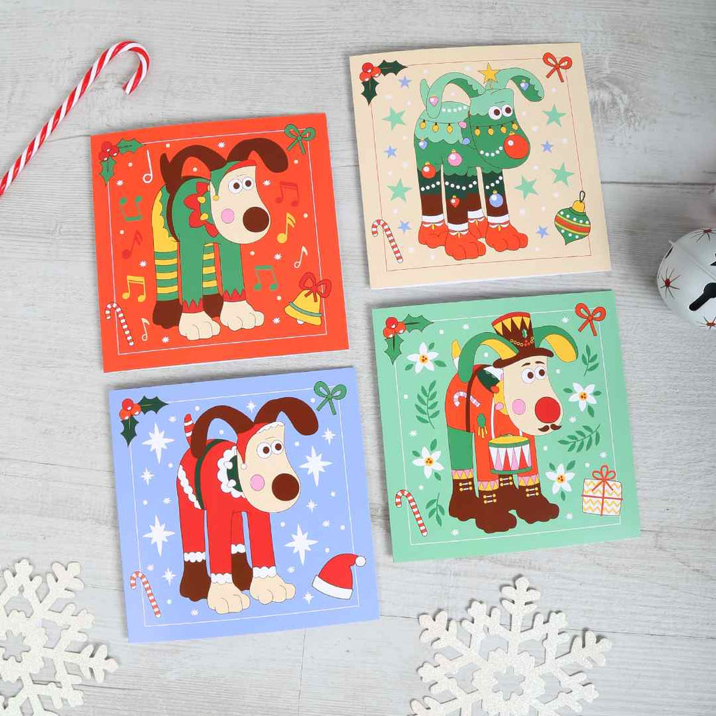 Four Christmas-themed greeting card designs featuring our favourite festive Gromit sculptures on a light wooden surface.