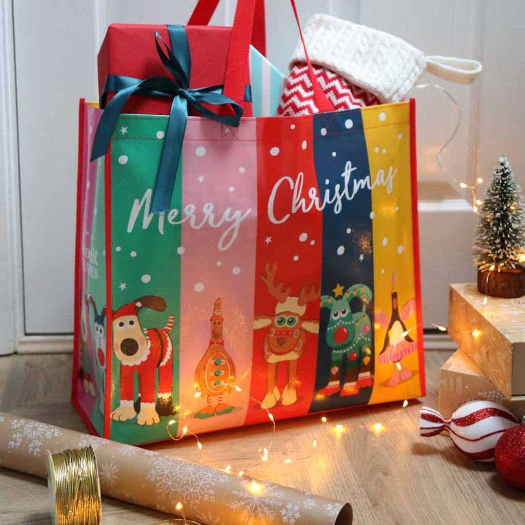 Colourful Christmas gift bag with Gromit Unleashed Christmas sculptures and 'Merry Christmas' text, surrounded by festive decor.