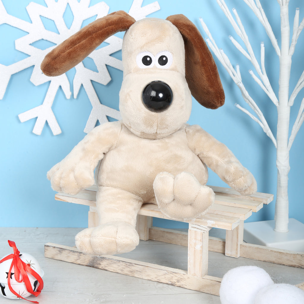 Plush Gromit soft toy on a small wooden sledge against a light blue background with decorative elements.