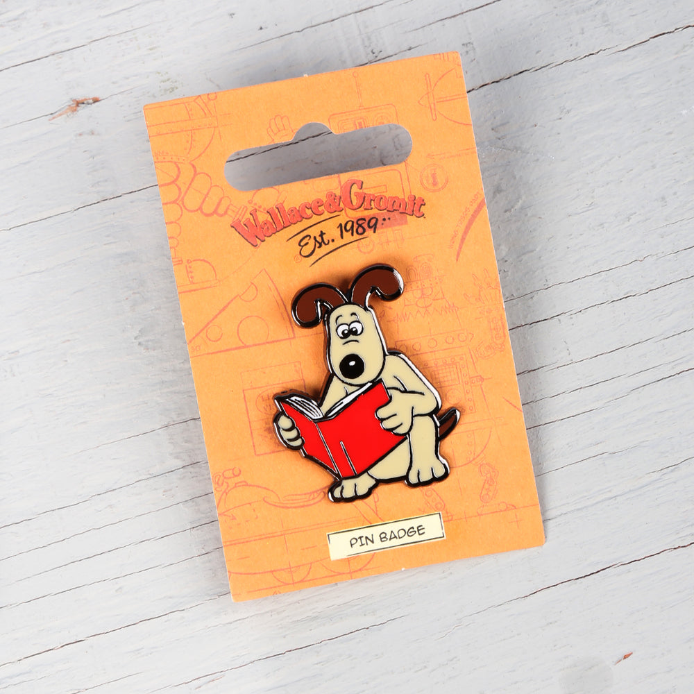 Enamel pin badge of Gromit reading a red book. 