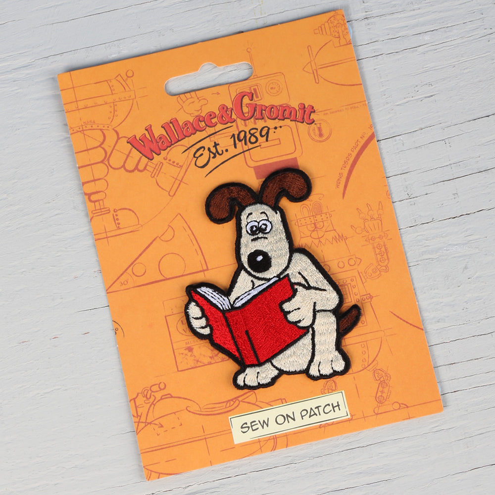 Gromit reading a red book sew on badge. 