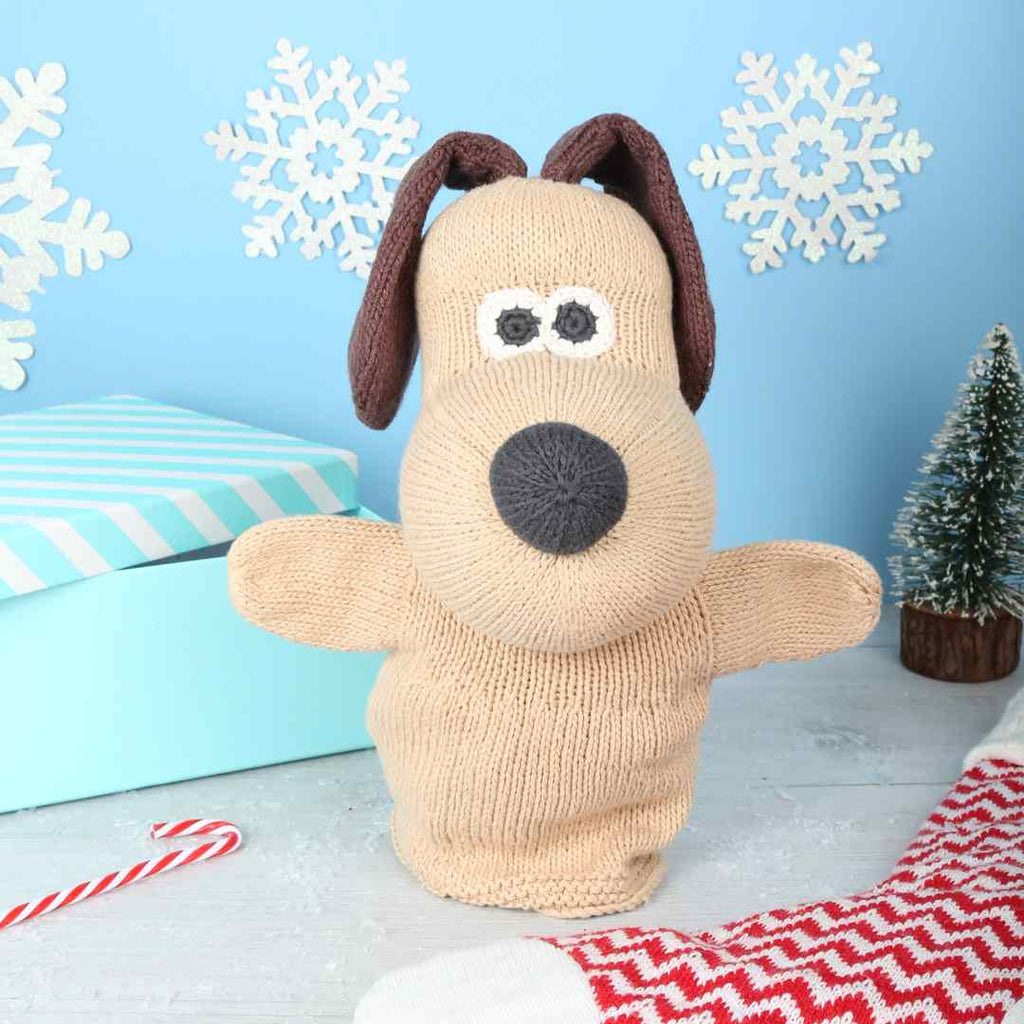 Knitted Gromit hand puppet  in a festive background with a stocking, a gift box and candy cane 