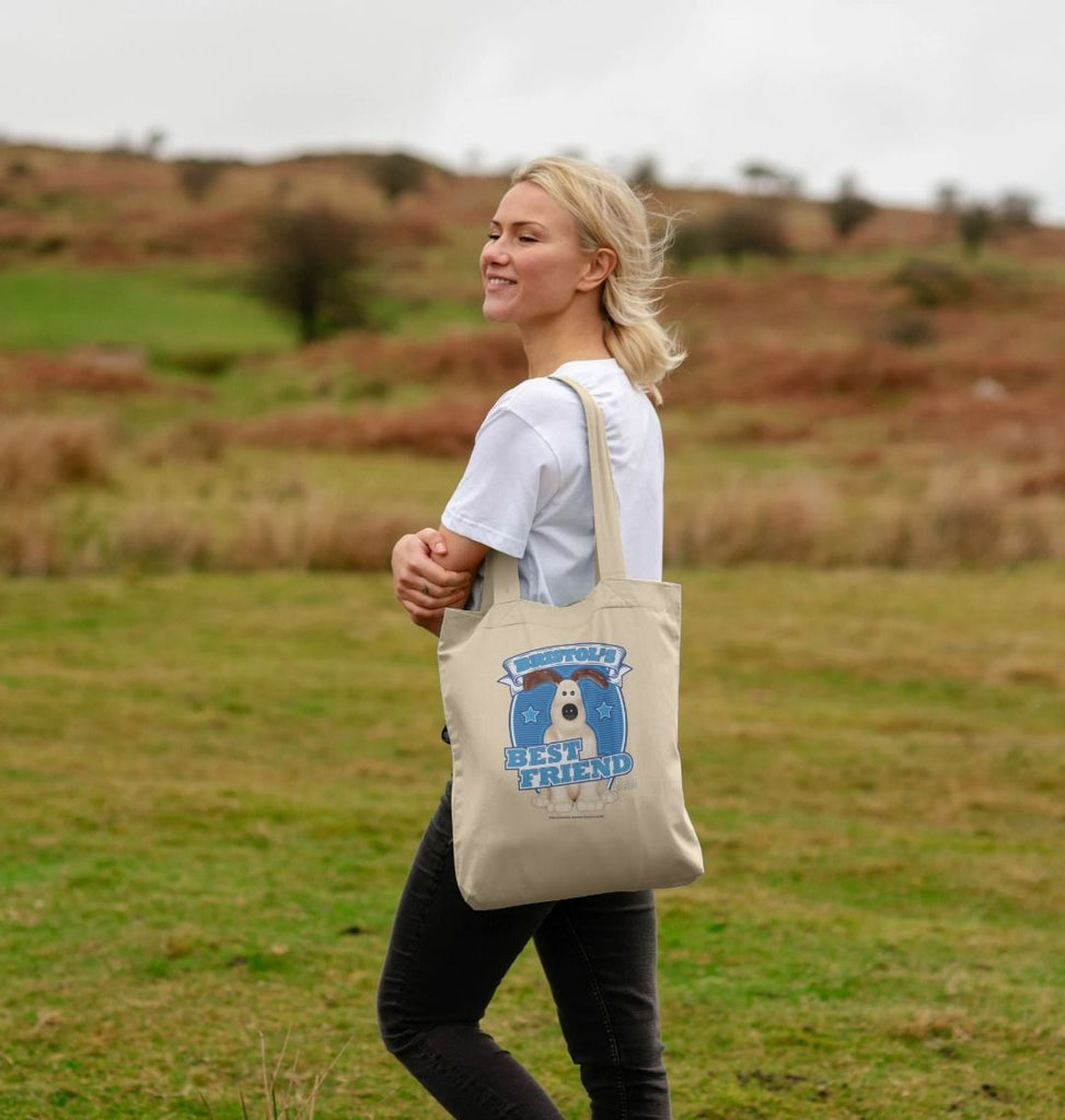 Blonde woman carrying a Bristol's Best Friend tote bag. Design features a blue background with the classic Gromit figurine in front. 