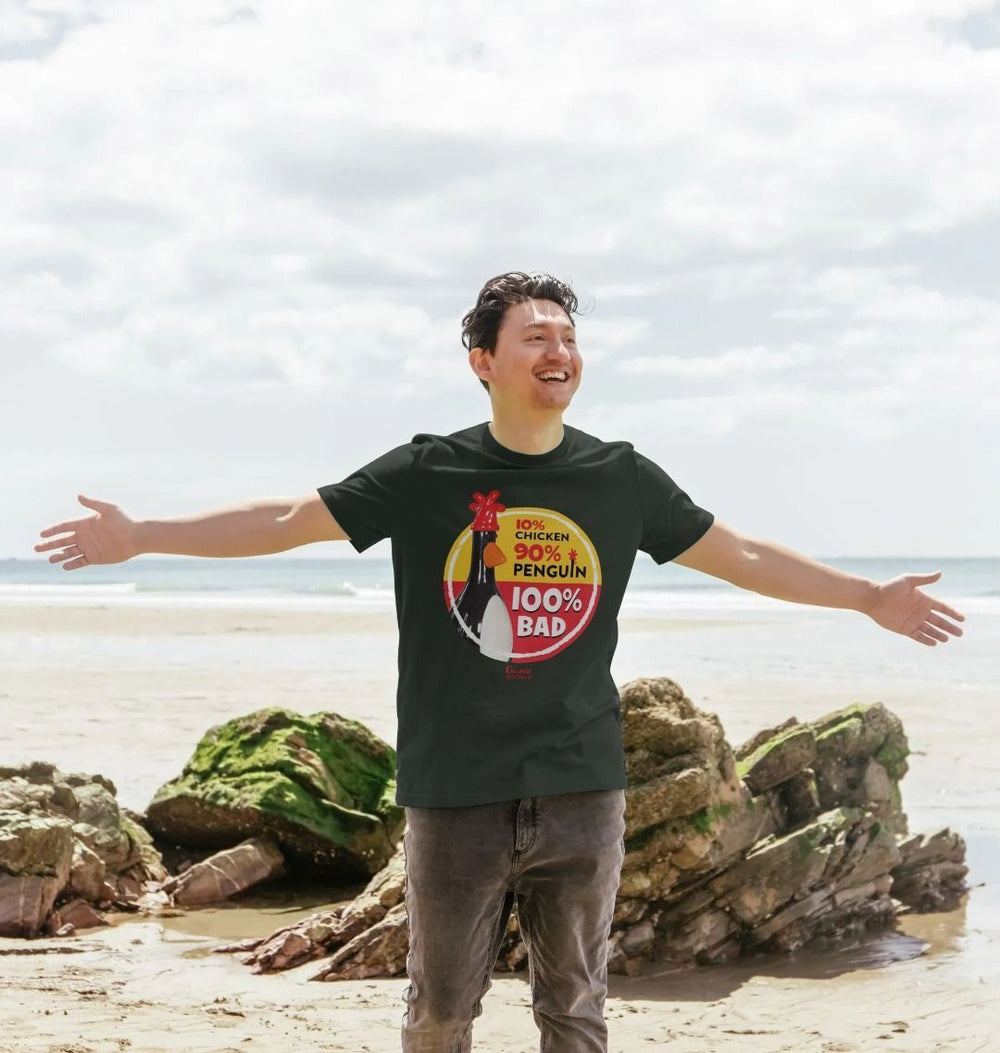 Man on a beach smiling and wearing Black 100% Bad Adult T-shirt with classic Feathers McGraw figurine in a red and yellow circle. Labelled 10% chicken 90% chicken and 100% bad. 